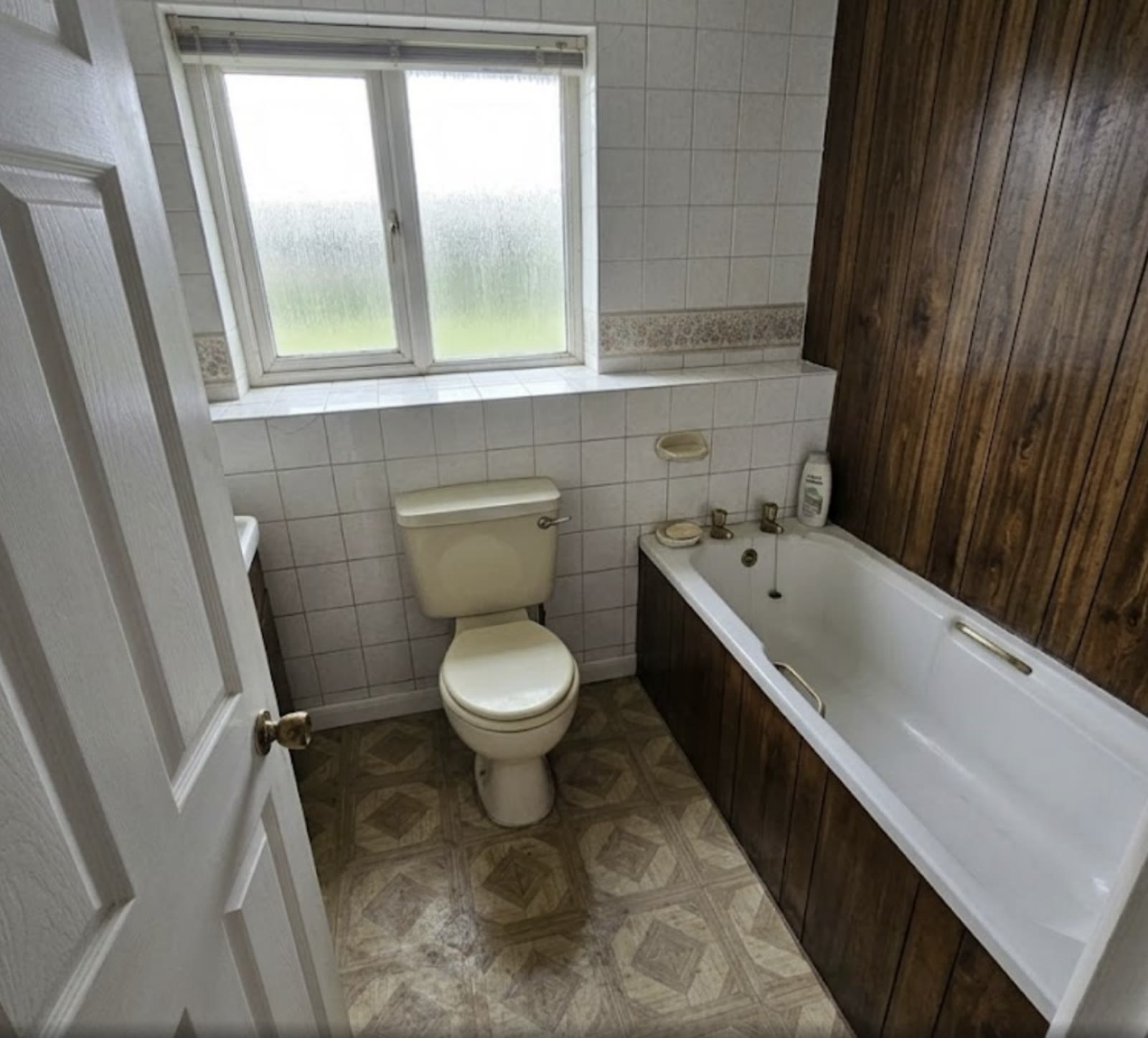 Before — original bathroom in Ighten Hill with dated tiles and wood panelling