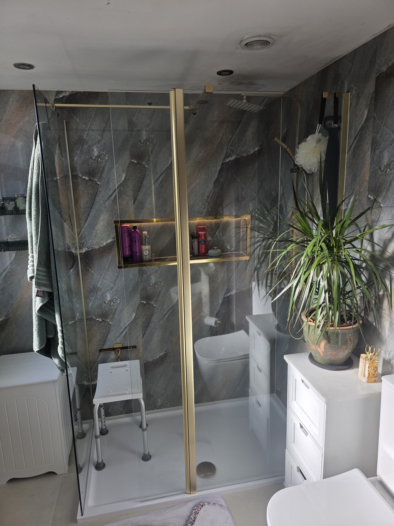 Walk-in shower with stone-effect PVC panels, brushed gold frame and lit niche