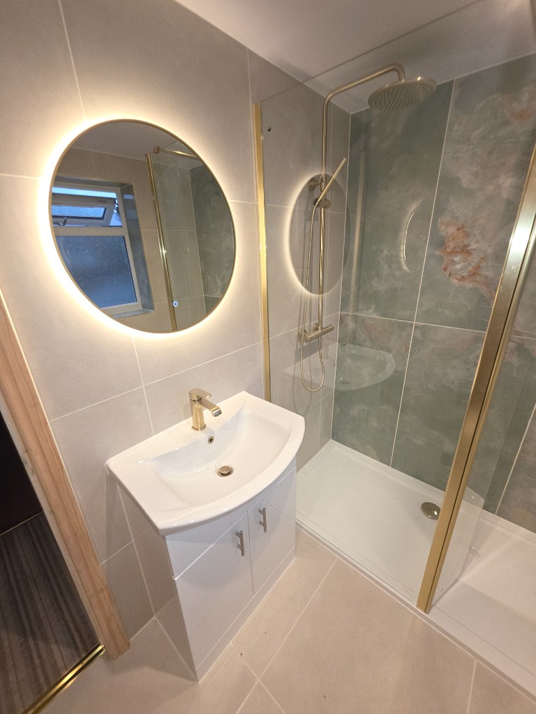 White vanity, backlit round mirror and gold-framed shower enclosure
