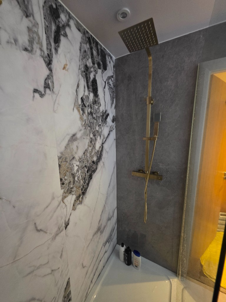 The Williams' panelled bathroom in Ramsbottom, with marble-effect boards and a brushed brass shower