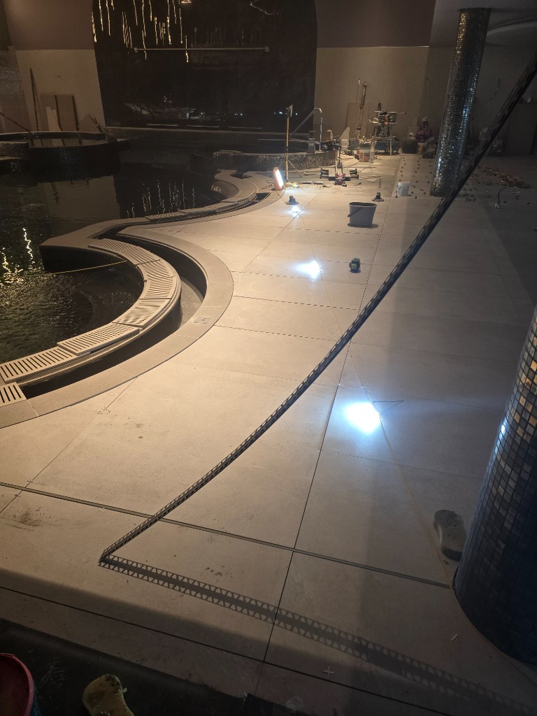 Work lights across freshly laid tiles beside the spa pool