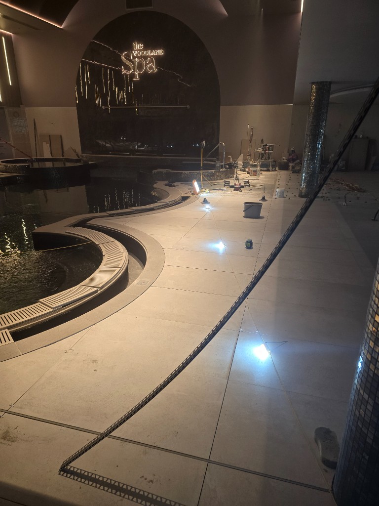 Large-format floor tiles around the curved pool edge at Woodland Spa