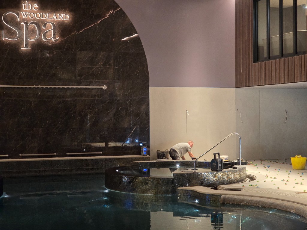 Tiler working beside the mosaic hot tub under the WOODLAND Spa sign